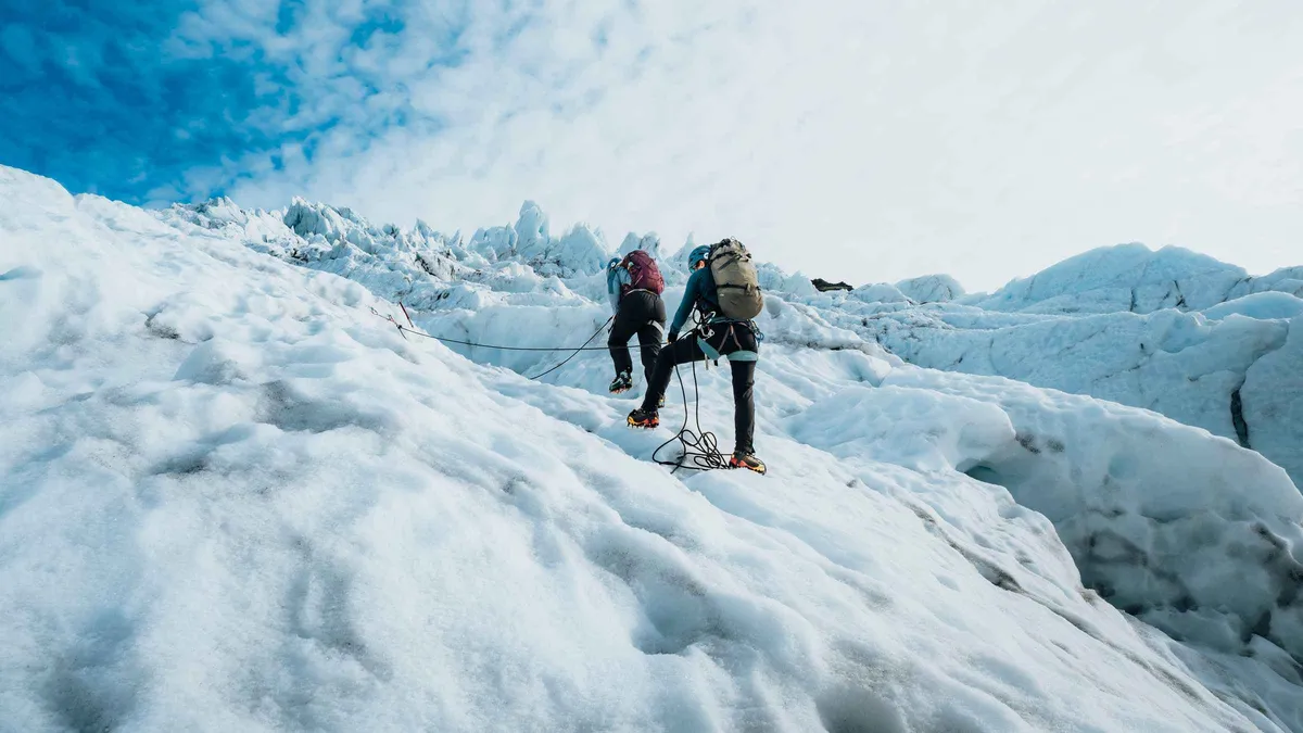 A climber swinging ice axes up a vertical blue ice wall on the Glacier XTreme Skaftafell glacier hike and ice climbing tour, Iceland